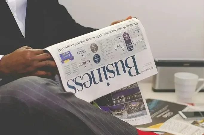 Betriebswirtschaftliche Beratung Mann in Anzug liest eine Zeitung, neben ihm stehen Pflanzen und ein Kaffeebecher.