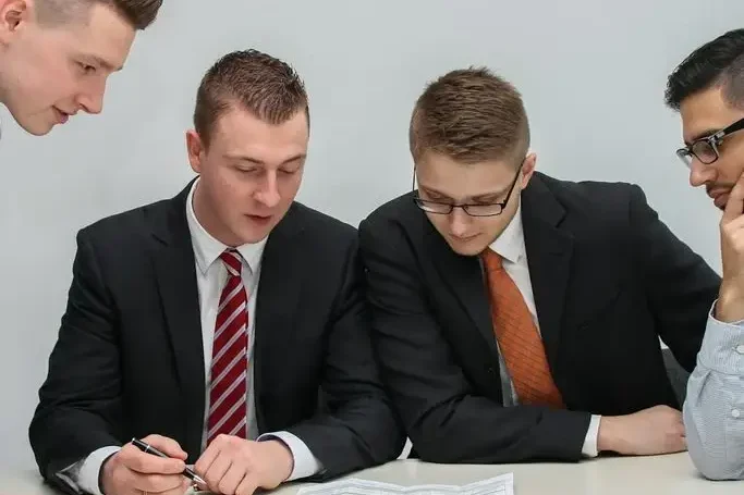 Planung und Kalkulation Vier Männer in Anzügen besprechen Dokumente am Tisch.